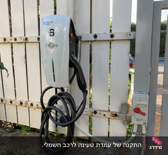 מטען לרכב חשמלי מותקן על גדר עץ לבנה